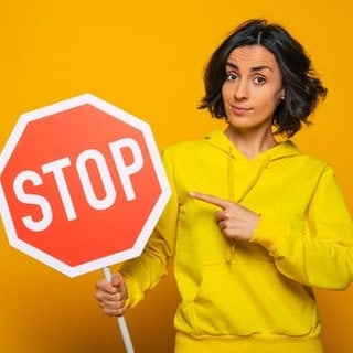 Junge Frau mit Stopp-Schild. Symbolbild für clevere Sprüche, um ein Gespräch zu beenden, bevor es zum Streit kommt.