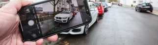 Eine Hand mit einem Smartphone fotografiert einen vermutlichen Falschparker um diesen anzuzeigen. | Symbolbild: Falschparker melden