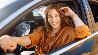 Junge Frau lächelt hinterm Steuer eines Autos. Symbolbild für das seltenste Verkehrszeichen in Deutschland, das kaum jemand kennt.