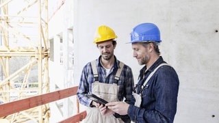 Zwei Handwerker auf einer Baustelle in Arbeitskleidung. Symbolbild für lustige Sprüche auf der Baustelle.