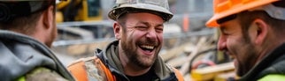 Arbeiter auf der Baustelle stehen zusammen und lachen. Symbolbild für lustige Sprüche auf der Baustelle.