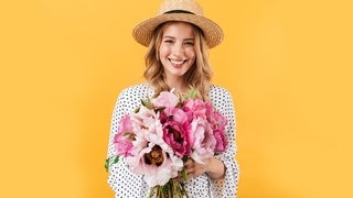 Junge Frau mit Sonnenhut und einem Straß Blumen in der Hand. Symbolbild für Sprüche, mit denen wir es durch die Blume sagen können, offiziell freundlich.