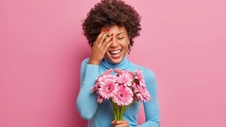 Junge Frau mit einem Straß Blumen in der Hand lacht. Symbolbild für Sprüche, mit denen wir es durch die Blume sagen können, offiziell freundlich.