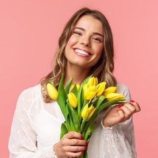 Junge Frau mit einem Strauß Blumen in der Hand lacht. Symbolbild für Sprüche, mit denen wir es durch die Blume sagen können, offiziell freundlich.