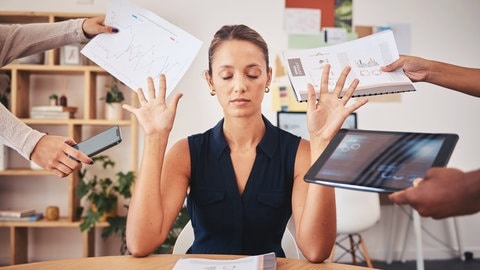 Frau sitzt im Büro und wehrt genervt mehrere Kollegen ab, die ihr neue Aufgaben geben wollen und sie kann nicht neinsagen