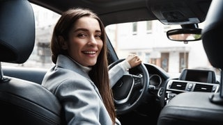 Junge Frau lächelt hinterm Steuer eines Autos. Symbolbild für das seltenste Verkehrszeichen in Deutschland, das kaum jemand kennt.