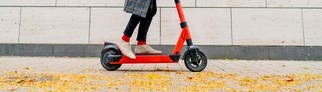 Mann mit E-Scooter auf Bürgersteig vor grauer Wand