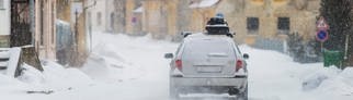 Ein Auto ist bei Schnee unterwegs in den Skiurlaub und hat eine Dachbox auf dem Dach