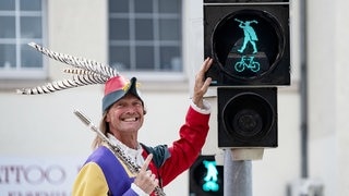 Der Rattenfänger von Hameln lächelt neben der Rattenfänger-Ampel in Hameln.