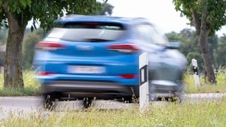 Auto fährt über eine Straße. Am Straßenrand stehen Reflektoren, Leitpfosten. Symbolbild für Artikel zum Verkehrszeichen und dessen Bedeutung.