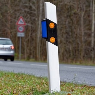 Auto fährt über eine Straße. Am Straßenrand steht ein Leitpfosten mit blauen Reflektoren, ein Wildwarnreflektor. Symbolbild für Artikel zum Verkehrszeichen und dessen Bedeutung für Autofahrer.