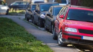 Rotes Auto parkt auf dem Gehweg. | Symbolbild für auf dem Gehweg parken: Ab wann gibts Bußgeld und sogar Punkte?