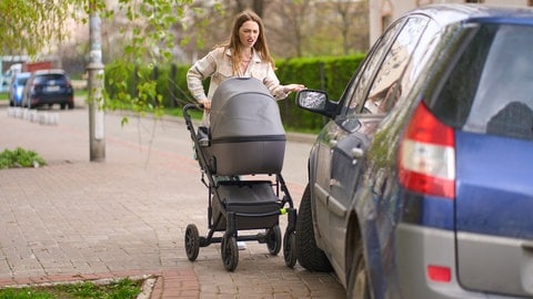 Frau spaziert mit Kinderwagen auf Gehweg und wird von geparkten Auto blockiert | Symbolbild für parken auf Gehweg: Wann gibt es Bußgelb und Punkt in Flensburg