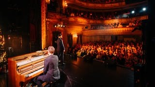 Mark Forster vor Publikum auf der Bühne des Theaters in Baden-Baden, mit Begleitung am Piano.