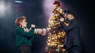 Anny Ogrezeanu, Gewinnerin der 12. Staffel "The Voice of Germany" mit Mark Forster, singend auf der Bühne vor beleuchtetem Weihnachtsbaum