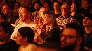 Publikum beim Konzert, junge Frau strahlt und die Menschen klatschen