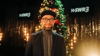 Mark Forster mit Brille und Cap vor Weihnachtsbaum