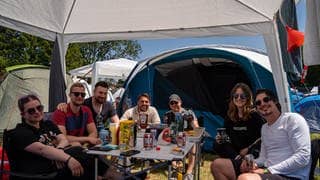Eine Gruppe Festivalbesuche von Rock am Ring 2023 sitzt auf dem Campingplatz am Tisch.