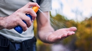 Eine Person sprüht sich Sonnenspray auf die Hand. Symbolbild für Stiftung Warentest Sonnencremes.