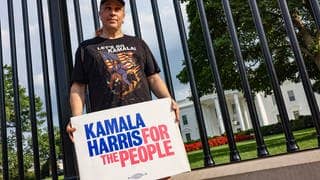 A man stands in front of the White House wearing a t-shirt and holding a sign endorsing Kamala Harris