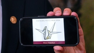 Jorgen Watne Frydnes, der Vorsitzende des Nobelkomitees, präsentiert auf seinem Smartphone das Logo der japanischen Organisation Nihon Hidankyō. Der Friedensnobelpreis geht in diesem Jahr an die japanische Organisation Nihon Hidankyo. Die auch als Hibakusha bekannte Organisation wird damit für ihre Bemühungen um eine Welt frei von Atomwaffen geehrt, wie das norwegische Nobelkomitee in Oslo bekanntgab.