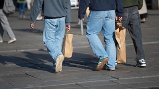 Drei junge Männer in Jeans gehen mit Einkaufstüten aus Papier durch die Innenstadt.