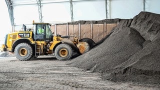 In einem Werk der Firma SWA Südwest Asphalt nimmt ein Bagger Recycling Material aus dem Straßenbau auf