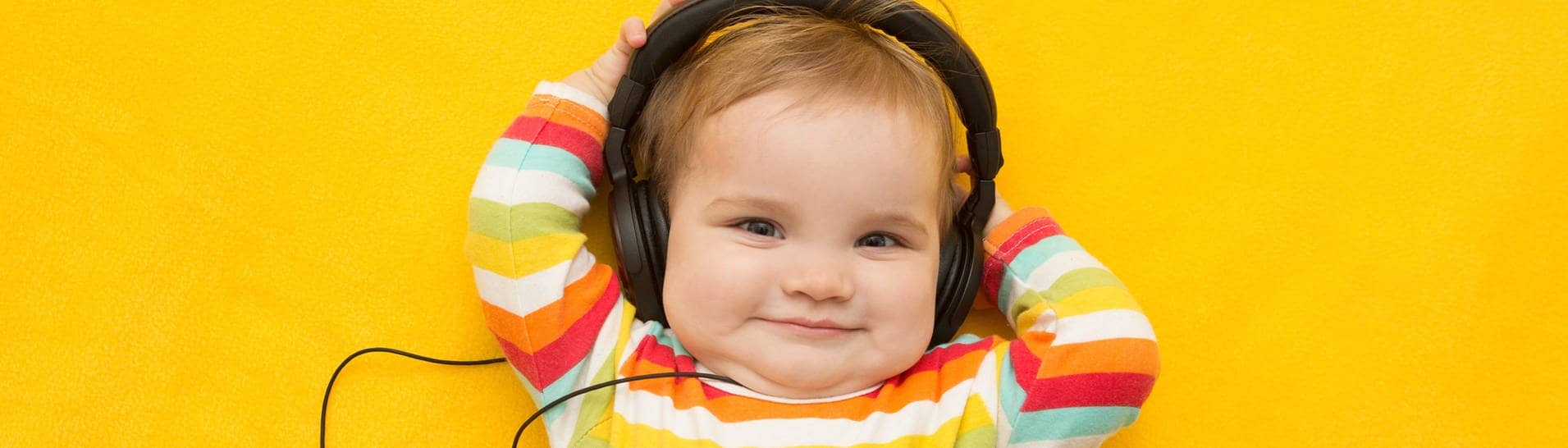 Ein Baby mit buntem Ringelpullover, das Kopfhörer trägt. Symbolisch steht das Bild für Musik, die Babies beruhigen soll.
