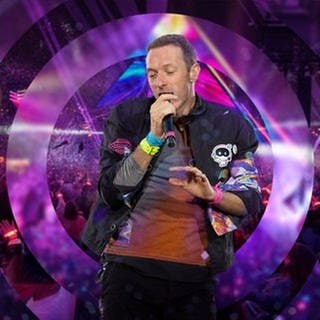 Chris Martin hält ein Mikrofon in der Hand, im Hintergrund ist das Publikum bei einem Coldplay-Konzert, für das ihr mit SWR3 Tickets gewinnen könnt