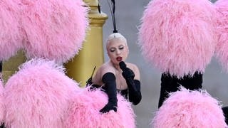 Lady Gaga tanzt umgeben von Tänzerinnen und Tänzer mit Federfächern am Ufer der Seine in Paris.