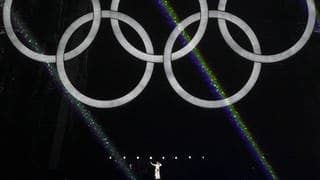 Celine Dion stoi pod Wieżą Eiffla i w błyszczącej białej sukni śpiewa klasyczną piosenkę Edith Piaf Under the Olympic Rings.