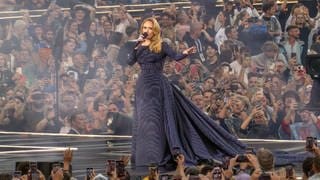 Sängerin Adele in langer Robe beim Konzert in München 2024. Sie läuft auf dem Bühnensteg singend durch Publikum.