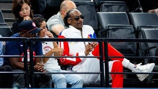 Snoop Dogg sitzt neben anderen Zuschauern und schaut sich das Turnen bei den Olympischen Spielen an