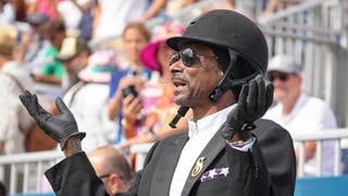 Snoop Dogg schaut sich im Reiterdress gekleidet bei den Olympischen Spielen das Dressurreiten an