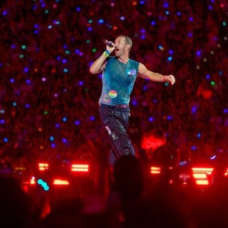 Chris Martin, Sänger der britischen Band Coldplay steht bei einem Konzert im Rahmen der „Music of the Spheres Tour 2024“ bei strömendem Regen in der Merkur auf der Bühne.