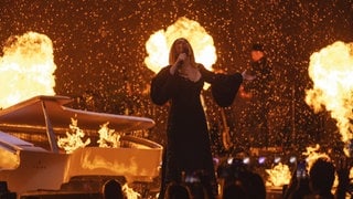 Adele singt bei ihrem vorerst letzten Konzert. Im Hintergrund sind Flammen zu sehen.