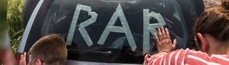 Rock am Ring: Zwei Menschen schieben ein Auto mit dem Schriftzug „RaR“.