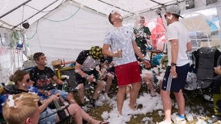 Festivalbesucher sitzen auf dem Campingplatz in einem Zelt und nutzen eine Schneemaschine.