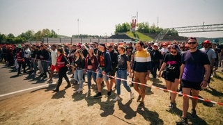 Viele Besucher bei Rock am Ring warten vor einer Absperrung darauf, dass sie auf das Festivalgeländer dürfen