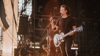 Sänger Tim von Rise Against hält den Mikrofonständer und schaut ins Publikum von Rock am Ring 2023