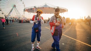 Zwei junge Männer sind auf dem Gelände von Rock am Ring unterwegs und tragen blaue Latzhosen