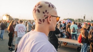 Auf dem Hinterkopf einer Person bei Rock am Ring sieht man Blumen, die in der Kurzhaarfrisur eingefärbt sind