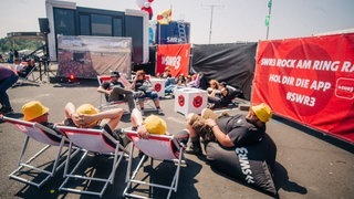 Einige Besucher von Rock am Ring ruhen sich in Liegestühlen von SWR3 aus