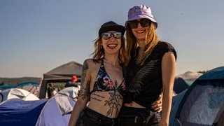 Zwei junge Frauen stehen vor Zelten auf dem Campingplatz von Rock am Ring