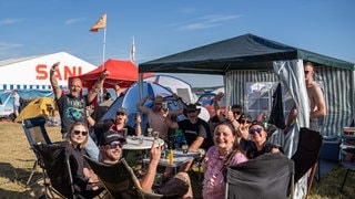 Ein Gruppe junger Menschen sitzt auf Campingstühlen im Kreis auf dem Zeltplatz von Rock am Ring