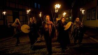 Frauen laufen in der Dunkelheit mit Fackeln, Trommeln und Waffen durch ein Dorf