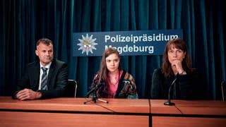 Polizeiruf-Kritik Magdeburg: Lana Stokowsky und Doreen Brasch vor Mikrofonen bei der Pressekonferenz. Im Hintergrund ein Schild mit Aufschrift Polizeipräsidium Magdeburg.