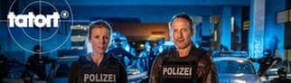 Julia Grosz und Thorsten Falke stehen in Einsatzkleidung nachts vor Polizeiautos und dem SEK