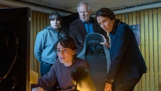 Szenenbilder aus dem Tatort „Borowski und das ewige Meer“. Das Ermittlerteam steht gebannt über PC-Bildschirme gebeugt und schaut darauf. Tatort-Checker Michael Haas spricht in seiner Kritik von einem „gechillten und zarten“ Krimi, obwohl es gleich eine ganze Mordserie gibt!