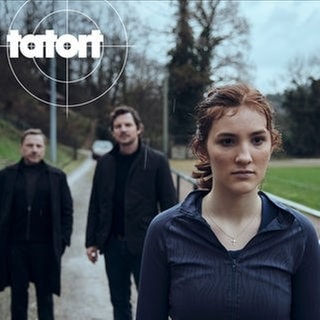 Szenenbild aus dem Tatort aus Stuttgart am 17.11. Emma Riedle ist die Schwester des Opfers. Sie steht im Vordergrund. Dahinter stehen Kommissare Thorsten Lannert und Sebastian Bootz